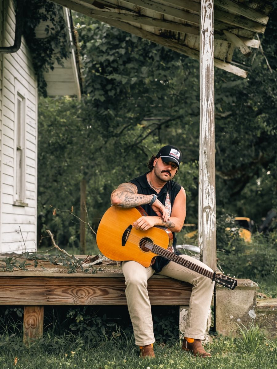 Tyler Evyns on a porch with an acoustic guitar