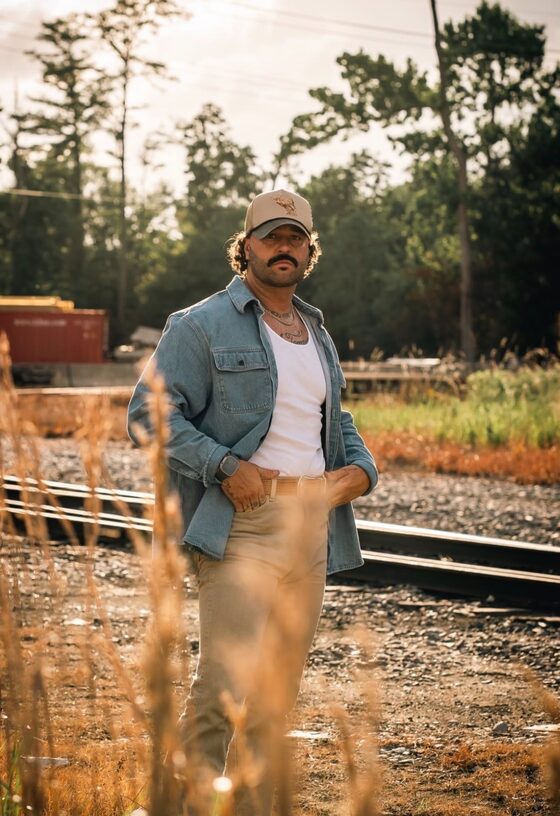 Tyler Evyns standing beside railroad tracks at golden hour